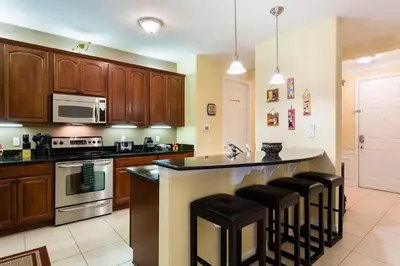 a kitchen with wooden cabinets and a island with bar stools at 3Br 2Bath Condo Balcony 5min Conv Center 2087ft in Orlando