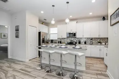 a kitchen with white cabinets and a large island with bar stools at Magical Memories Await at Jimmy Cricket's Retreat in Kissimmee