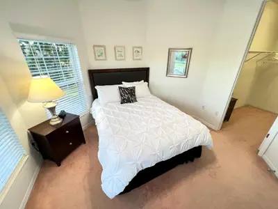 a bedroom with a bed and a lamp and a window at Mickeys Homestead - Stylish 4BR Lakefront Cottage with Huge South Facing Pool Hot Tub BBQ - 2 miles Disney! in Orlando
