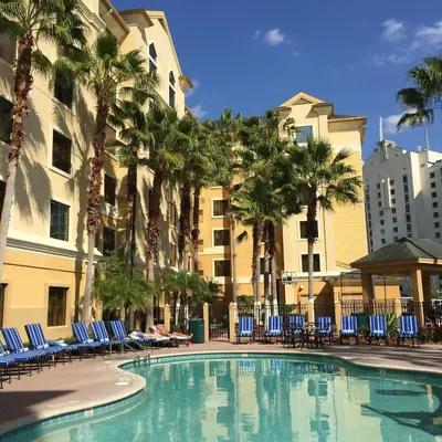 a swimming pool with chairs and palm trees and a building at staySky Suites I-Drive Orlando Near Universal in Orlando
