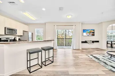 a kitchen with white cabinets and a counter with stools at Upstay Condo with Outdoor Pool & Sauna in Orlando