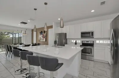 a white kitchen with a large white island with bar stools at American Secret 10 BED 7 Miles to Disney in Kissimmee