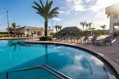 a large swimming pool with chairs and palm trees at Storey Lake home close to Disney and other parks in Kissimmee