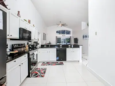a white kitchen with white cabinets and black appliances at Casita mi Encanto a Cozy & Spacious House, 4-bedroom 3-Bath & pool in Kissimmee