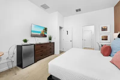 a white bedroom with a bed and a flat screen tv at Fresh Amazing Family Home. Private Pool. Game Room. Sleeps 24 in Kissimmee