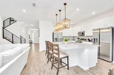 a kitchen with white cabinets and a large island with chairs at Upstay 9BR Disney Retreat w Pool, BBQ & Hot Tub in Kissimmee