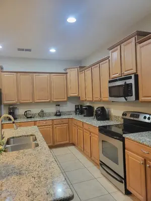 a large kitchen with wooden cabinets and a microwave at Paradise Villa Disney Staycation Pool, Fun & Resort Access in Kissimmee