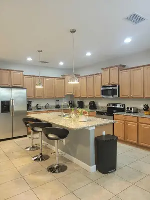 a kitchen with wooden cabinets and a island with bar stools at Paradise Villa Disney Staycation Pool, Fun & Resort Access in Kissimmee