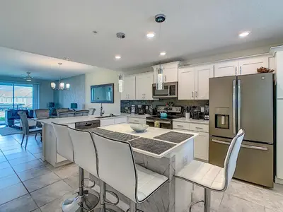 a kitchen with white cabinets and a kitchen island with chairs at Luxury Brand NEW 2 bedroom apt near DISNEY! in Kissimmee