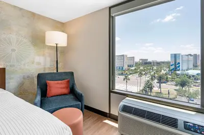 a bedroom with a large window with a chair and a television at Cambria Hotel Orlando near Universal Theme Parks in Orlando