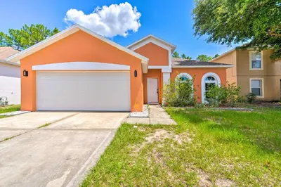 a house with an orange garage in a yard at Sunny Clermont Retreat with Lanai 12 Mi to Disney! in Orlando