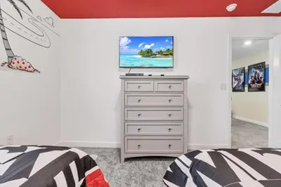 a bedroom with a bed and a dresser with a tv on it at Delight Indoor Adventure Steps From Disney in Kissimmee