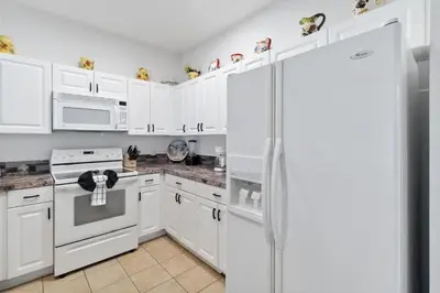 a white kitchen with white cabinets and a refrigerator at Huge Screened Patio That Overlooks Lake Buck, Near Famous Attractions!! in Orlando
