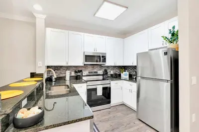 a kitchen with white cabinets and a stainless steel refrigerator at 2BR Condo with Pool - Near Disney in Orlando