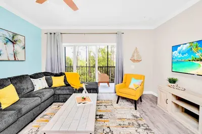 a living room with a gray couch and a yellow chair at 2BR Condo with Pool - Near Disney in Orlando