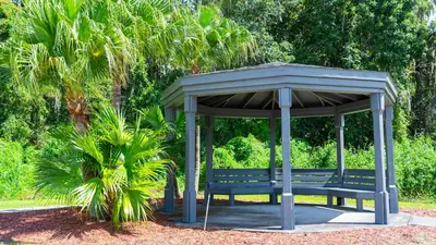 a park bench sitting under a canopy next to a palm tree at Enchanting Escape 3 Bedroom Minutes from Disney! in Kissimmee