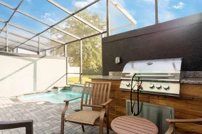 an outdoor kitchen with a grill and a swimming pool at Amazing Cozy Private Pool - 4404 in Kissimmee