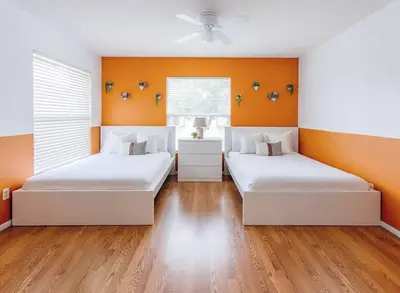 two beds in a room with orange walls and wooden floors at Orlando Boho Villa in Kissimmee