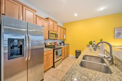 a kitchen with a stainless steel refrigerator and wooden cabinets at 5 Mi to Disney Paradise Palms Retreat with Lanai in Kissimmee