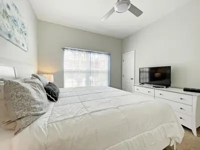 a white bedroom with a bed and a flat screen tv at Candy Palm townhouse in Kissimmee