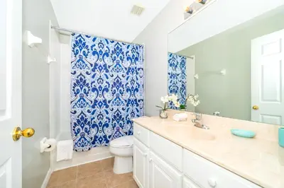 a bathroom with a toilet and a blue and white shower curtain at Emerald Island Escape- Pool and spa in Kissimmee