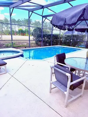 a table and chairs with an umbrella next to a swimming pool at Luxury 5 Bedroom Villa with Secluded Pool/Spa in Glenbrook community near Orlando in Orlando