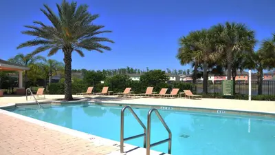a swimming pool with chairs and palm trees at Coral Cay - 4 Bed 3 Baths Townhome in Kissimmee
